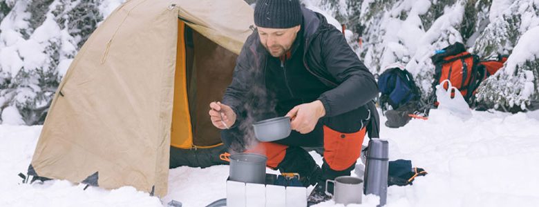 درحال آشپزی در کوهستان برفی در مقابل چادر